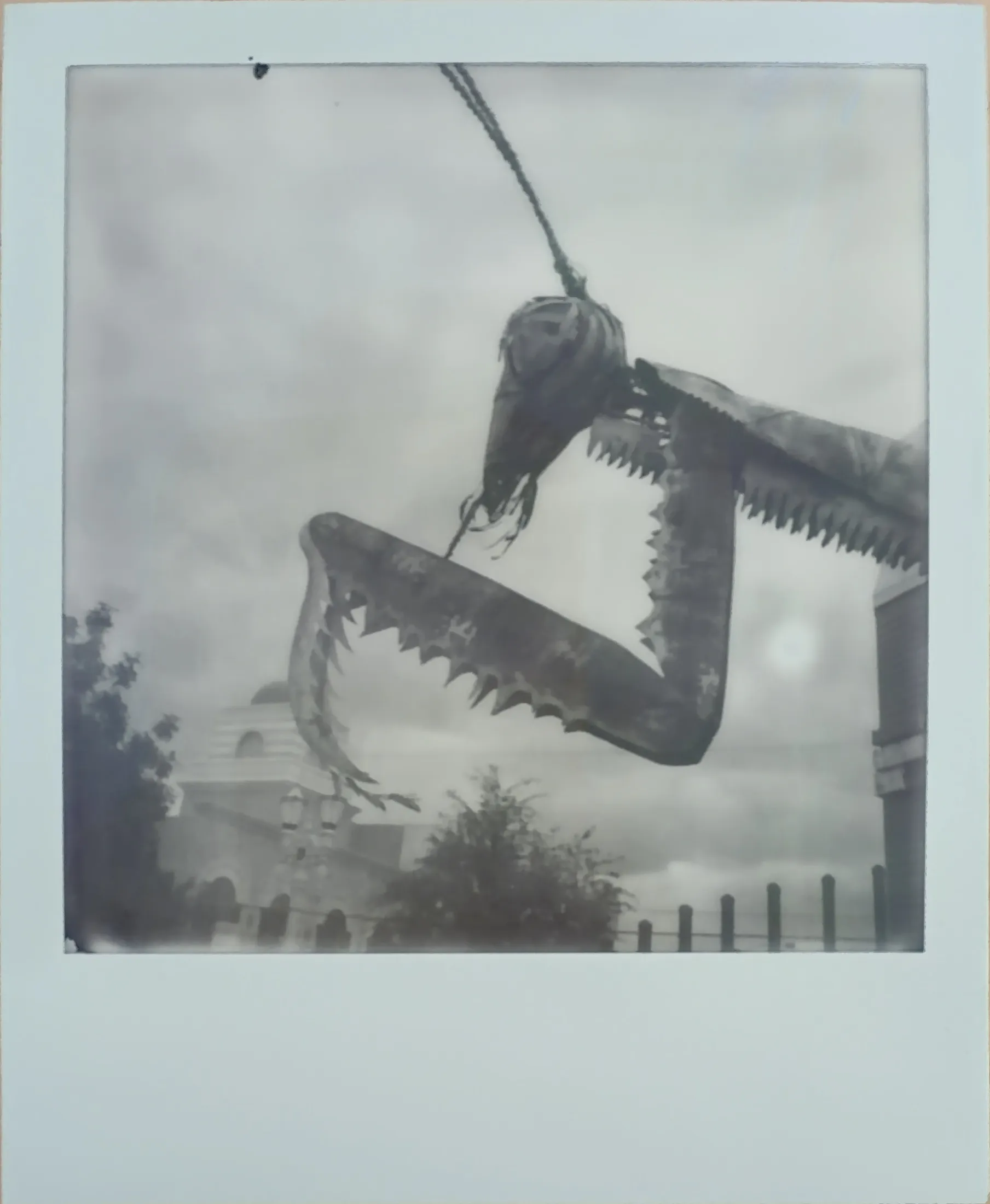 A black and white print of a giant metal praying mantis sculpture against a cloudy sky