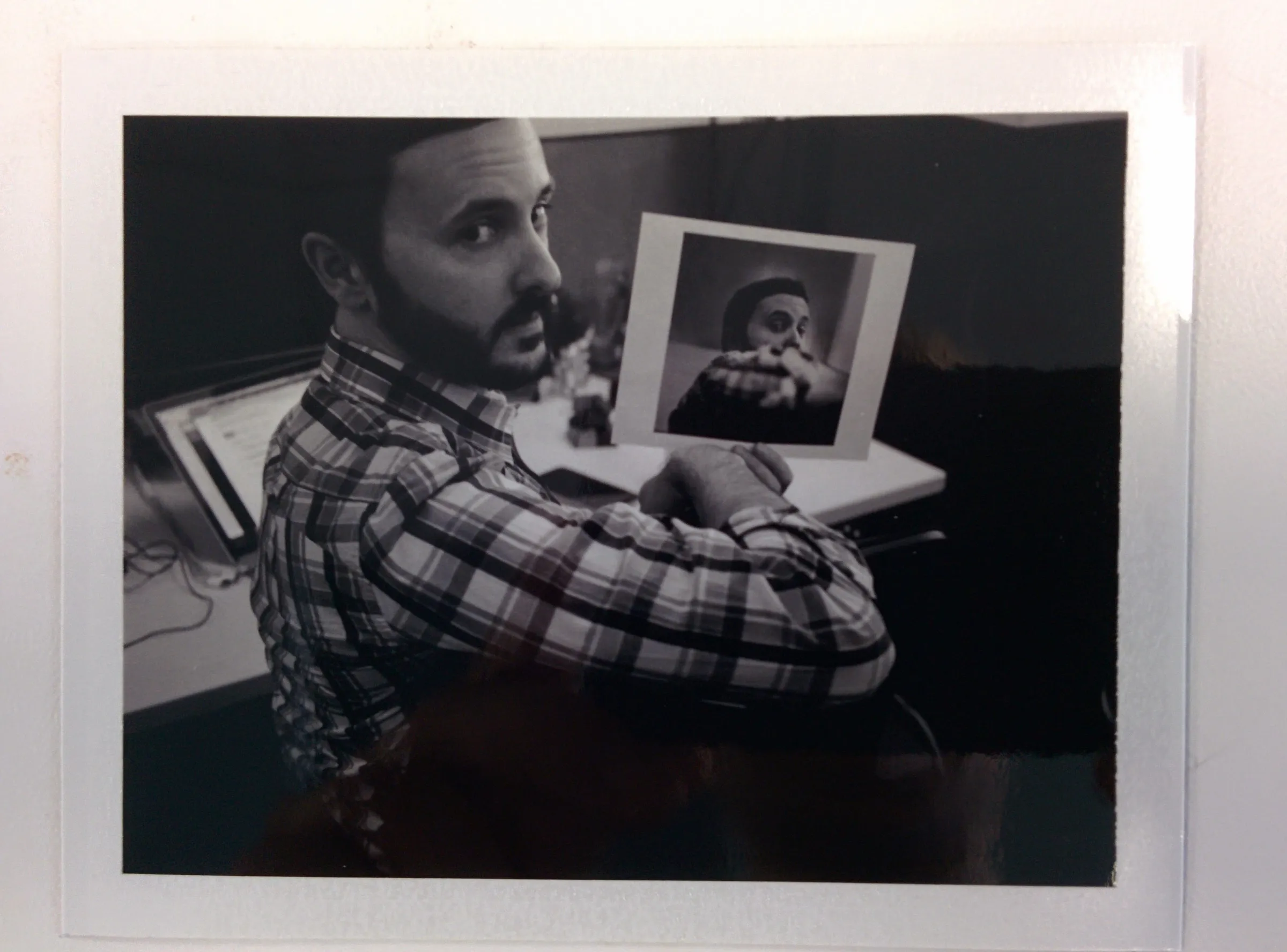 A black and white peel-apart print of a man at a desk holding up a print of himself