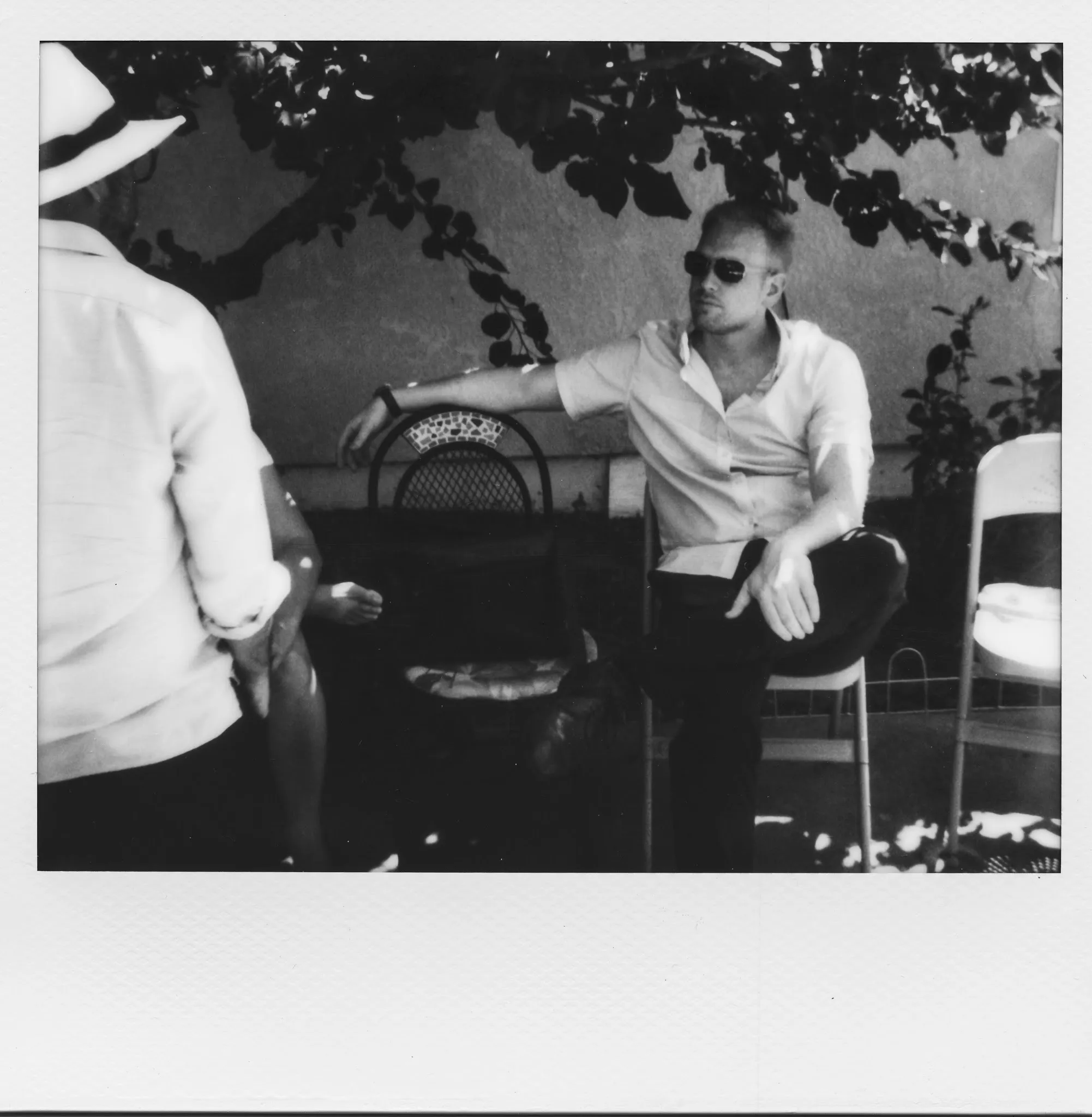 A black and white Spectra print of two men talking under a vine in a garden