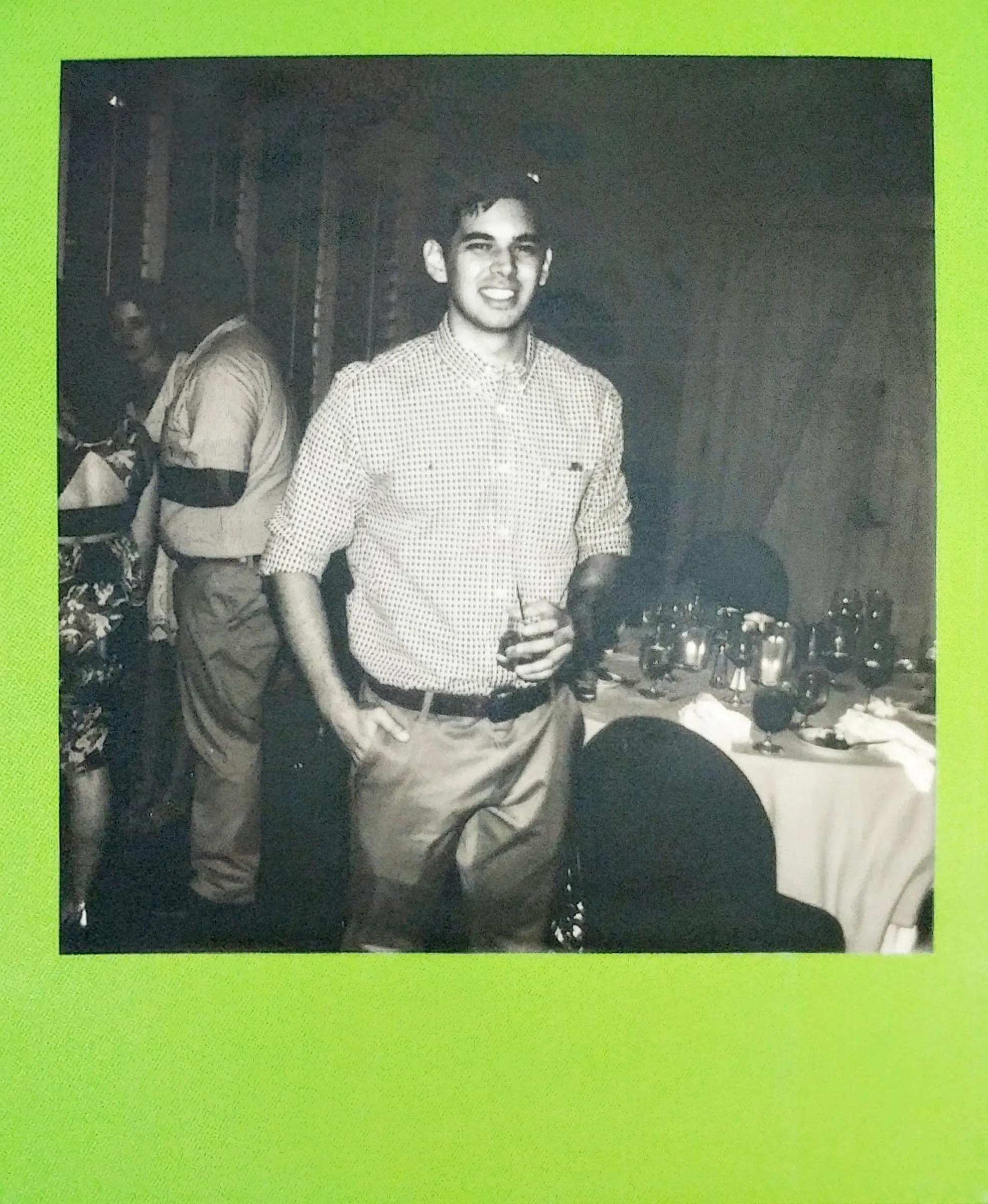 A black and white print in a green frame of a smiling wedding guest holding a drink